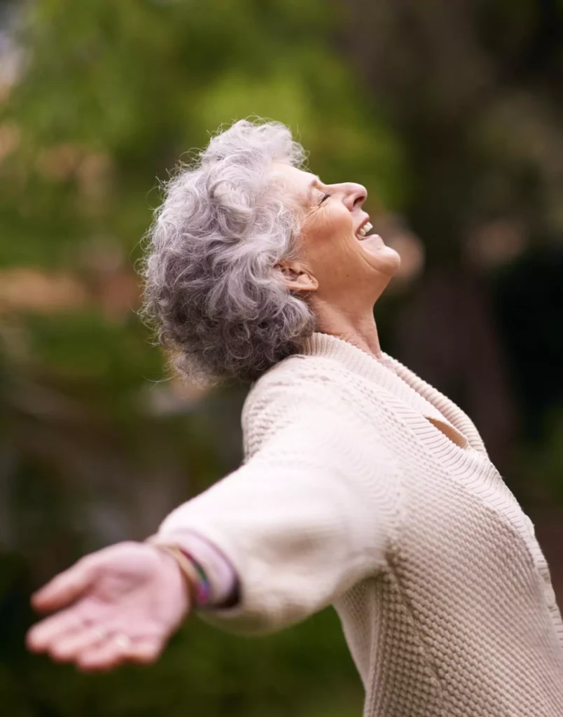 Breathe helped this elderly woman feel free again, shown smiling with arms wide open in nature.